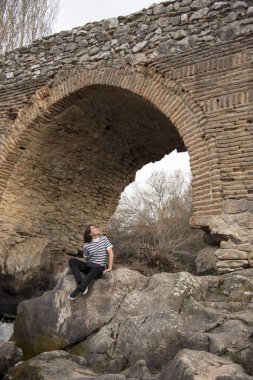 Tarlada poz veren ve arka planda köprüsü olan genç bir adam. Açık havanın tadını çıkarıyorum.