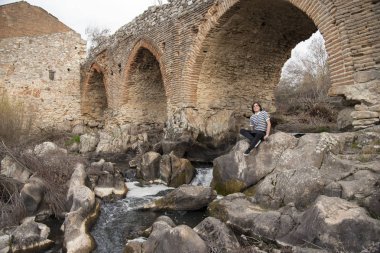 Tarlada poz veren ve arka planda köprüsü olan genç bir adam. Açık havanın tadını çıkarıyorum.
