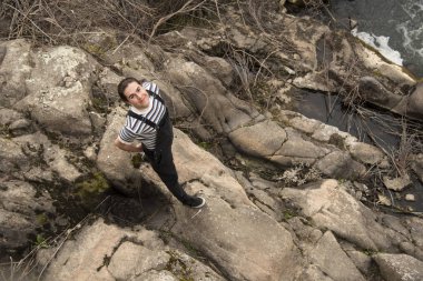 Genç adam tarlada poz veriyor ve arkada bir köprü var.