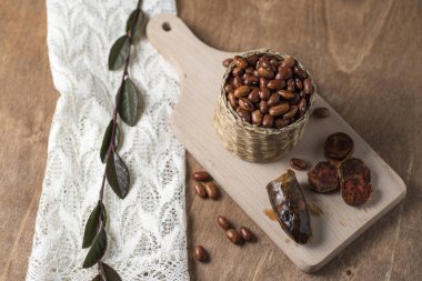 Tahtadaki siyah fasulyelerle dolu bir tencere, bir parça sosisin yanında.