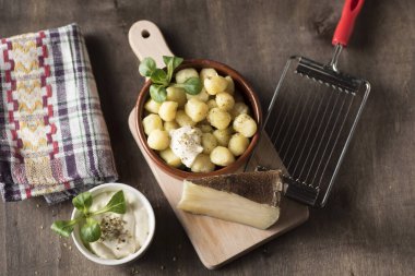 Lezzetli bir tabak yuvarlak patates gnocchi yanında peynir sosu ve onları tatmak için gerekli aksesuarlar.