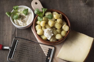 Lezzetli bir tabak yuvarlak patates gnocchi yanında peynir sosu ve onları tatmak için gerekli aksesuarlar.