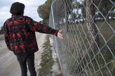 Genç adam sırtüstü yürüyor toprak bir yolda, çitin yanında.