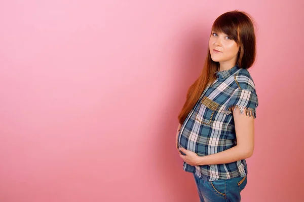 Mulher grávida em jeans e camisa xadrez segurando sua barriga — Fotografia de Stock