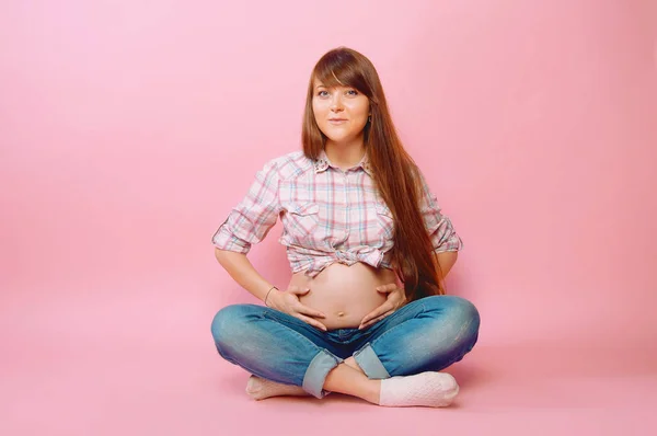 Femme enceinte en jeans et chemise à carreaux assis jambes croisées — Photo