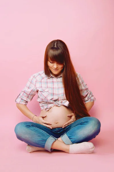 怀孕的妇女，穿着牛仔裤和格子的衬衫，抱着她的肚子 — 图库照片