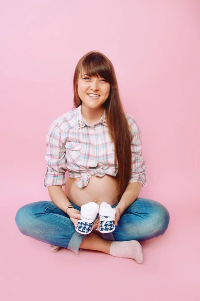 Mulher grávida em jeans e camisa xadrez sentado com a perna cruzada — Fotografia de Stock