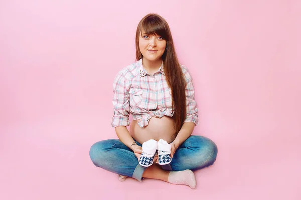 Těhotná žena v džínách a kostkovanou košili, sedí se zkříženýma nohama — Stock fotografie