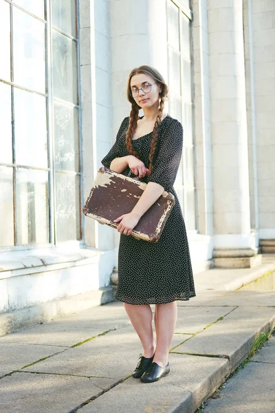 Молодая студентка с чемоданом и длинными косичками — стоковое фото