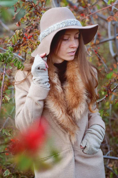 Roztomilá zrzka žena mezi keři jeřabinovo fedora klobouk — Stock fotografie