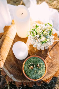 Ahşap masada, üzerinde mumlar, alyanslar ve gelin buketi olan bir masa.
