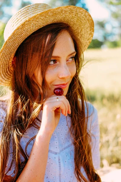 若いです女性でわら帽子食べるチェリー屋外 — ストック写真