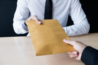 İş adamı, rüşvet parasını kahverengi bir zarfla alır. Ofiste başka bir adam, rüşvet ve yolsuzluk kavramı oluşturur..