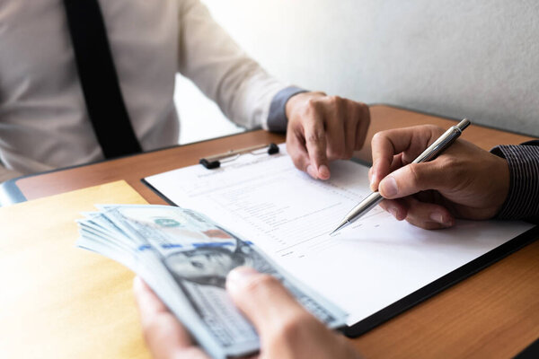 The businessman signed a contract agreement documents and receive a bribe from another businessman sitting in front at the office, Bribery and corruption concept.