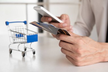 Kredi kartı tutan, cep telefonu kullanan, online alışveriş yapan bir adamın eli..