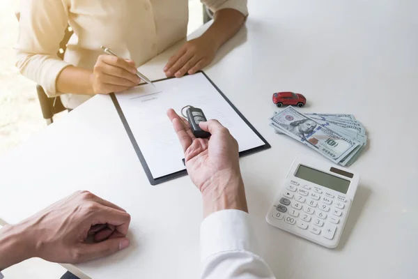 Customer is signing the car rental agreement and getting a car key from dealer after signed in the office, Car rental concept.