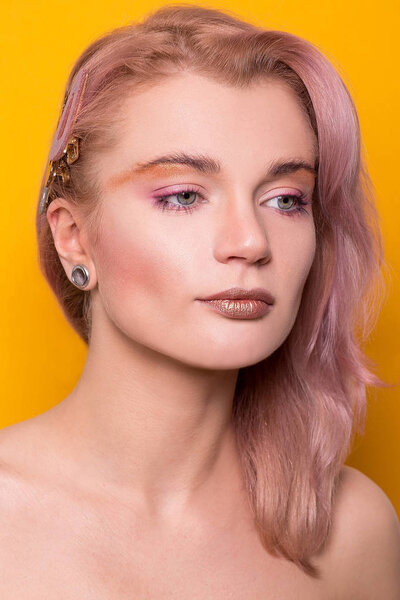 Сияющий золотой макияж на красивой молодой европейской модели девушки, изолированной на оранжевом фоне в фотостудии
