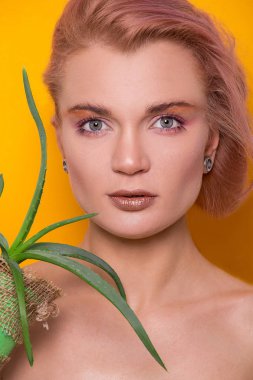 Bir fotoğraf stüdyosundaki turuncu bir arka planda, elinde aloe parçasıyla gezen güzel Avrupalı genç bir kızın parlak makyajı.