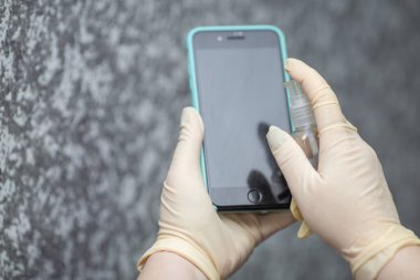 Kadının eli cep telefonuna alkol, dezenfektan spreyi sıkıyor, Covid-19 virüsü enfeksiyonunu önlüyor, mikrop ya da bakteri bulaşmasını önlüyor, ortadan kaldırmak için silmek ya da temizlemek için telefon kullanıyor, Coronavirus salgını