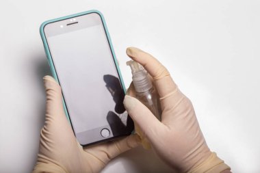 Kadının eli cep telefonuna alkol, dezenfektan spreyi sıkıyor, Covid-19 virüsü enfeksiyonunu önlüyor, mikrop ya da bakteri bulaşmasını önlüyor, ortadan kaldırmak için silmek ya da temizlemek için telefon kullanıyor, Coronavirus salgını