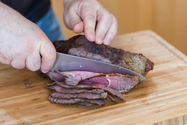 Slicing juicy Roast beaf with knife on wooden cutting board