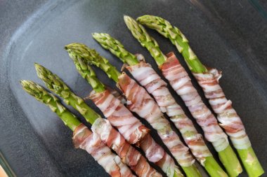 Siyah pan zemin üzerine pastırma ile sarılı ızgara yeşil kuşkonmaz