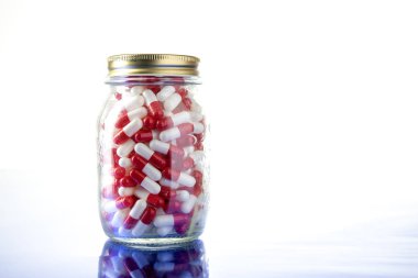 Beyaz ve kırmızı iyileştirici haplar içeren cam kavanoz.