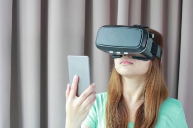 Evde sanal gerçeklik gözlüklü genç kadın.