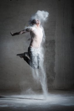 Gri arka planda uçan unla atlayan erkek model. Uçan un. Yaratıcı, alışılmadık, moda, cazibe, mor saç, poz, moda, sanat, sanat, hareket, dans