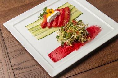 Beyaz kare tabakta kırmızı balık sebzeli ve salatalı güzel bir yemek. Yemek, deniz ürünleri, lezzetli, güzel, restoran, servis, yemek, diyet, sağlıklı beslenme.