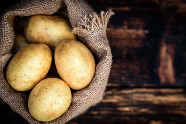Raw potatoes in a linen bag on dark wooden background with copy space.