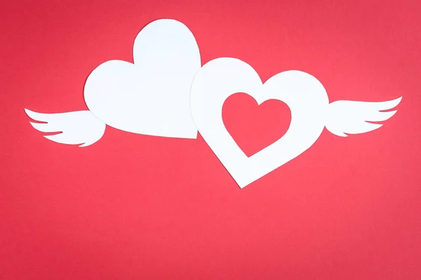 Two white paper hearts with wings on red back ground with copy space. Valentine\'s day concept.