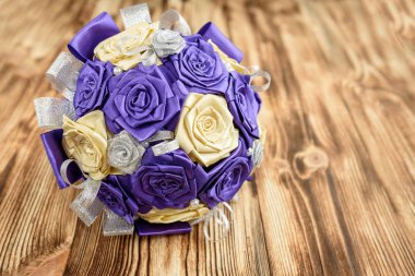 Gelin buketi mor, bej ve gümüş renkli suni güller ahşap masadaki saten kurdelelerden kopyalanmış..