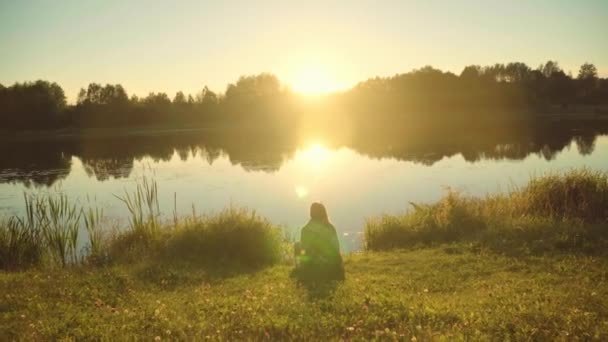 Jonge Vrouw Zit Bij Het Meer Tijdens Zonsondergang — Stockvideo