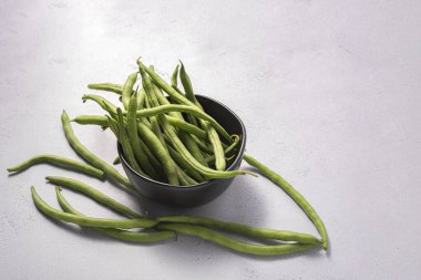 Taze çiğ fasulye, siyah bir kâse içinde beyaz bir yüzey üzerinde..