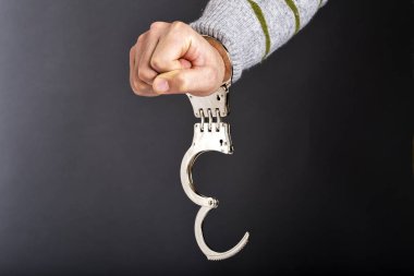 Closeup of unlocked handcuffs hanging on man hand isolated on gray background clipart