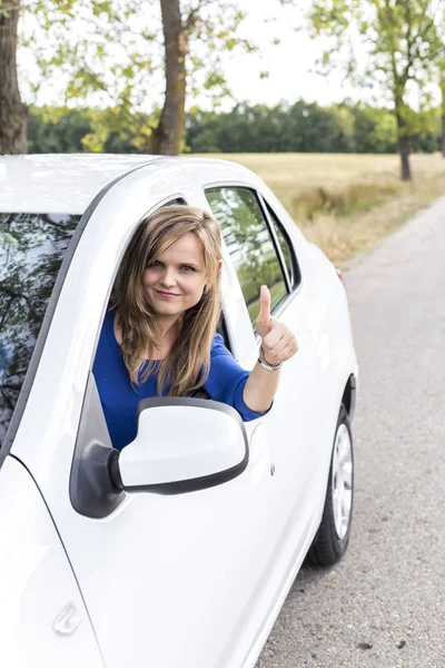 快乐的年轻女人 手握大拇指在新车的轮子上 — 图库照片
