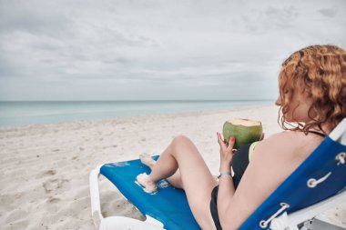 Kumsalda hindistan cevizi sütü içen kadın.