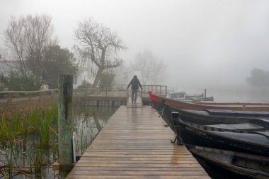 Catarroja limanında sisli bir günde ahşap bir geçitte bir adam. Valencia İspanya.