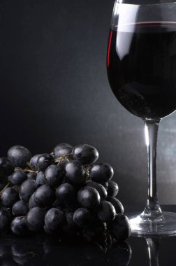 Koyu arkaplanda üzümlerin yanında bir kadeh kırmızı şarap. Dikey fotoğraf. Yakın plan..