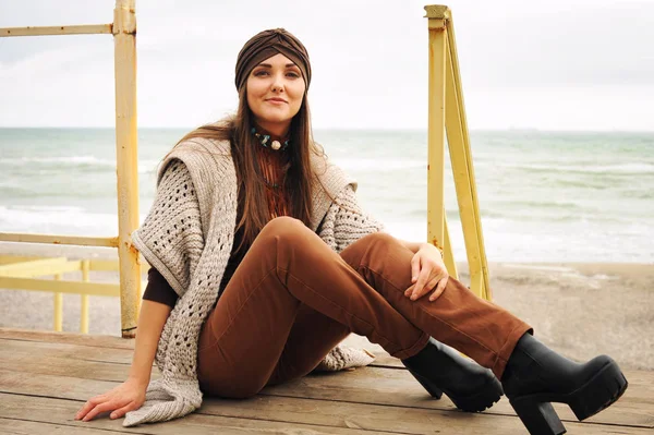 Retrato de moda de uma linda mulher morena sorridente sentada em frente à praia da cidade, sorrindo e olhando para a câmera — Fotografia de Stock