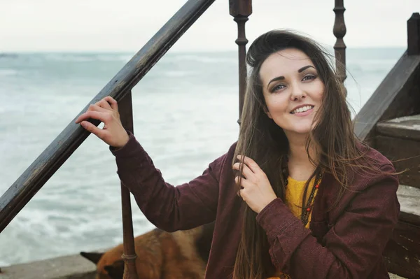 Linda mulher morena sorridente sentada em uma escada contra a paisagem marinha, sorrindo e olhando para a câmera — Fotografia de Stock