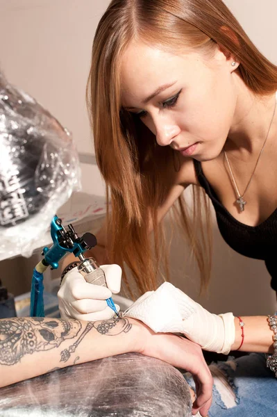 Vacker ung flicka tatuering konstnär porträtt under skapandet tatuering på en mans hand. — Stockfoto