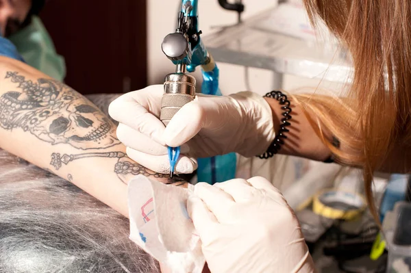 Girl tattoo artist portrait during creation tattoo on a man`s hand under the lamp light — Stock Photo, Image