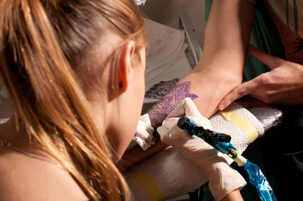 Mistrzyni tatuażu kobieta robi tatuaż na dłoni na fioletowym niebieskim podobieństwie przyszłego tatuażu — Zdjęcie stockowe