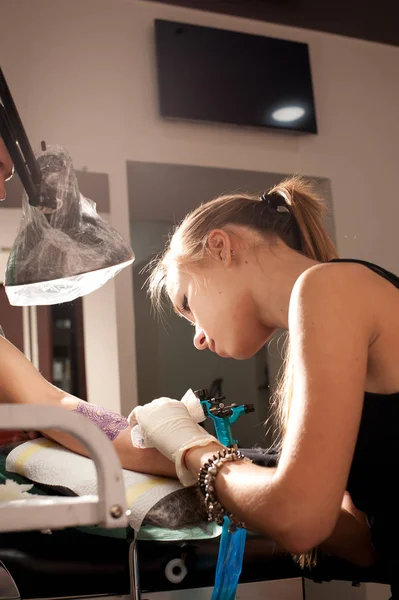 Retrato de uma jovem mulher bonita mestre tatuador faz a tatuagem na mão em uma semelhança azul arroxeada de uma futura tatuagem — Fotografia de Stock