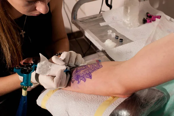 Flicka tatuerare gör tatuering på en hand mot blå avbild av en framtida tatuering med en skiss. — Stockfoto