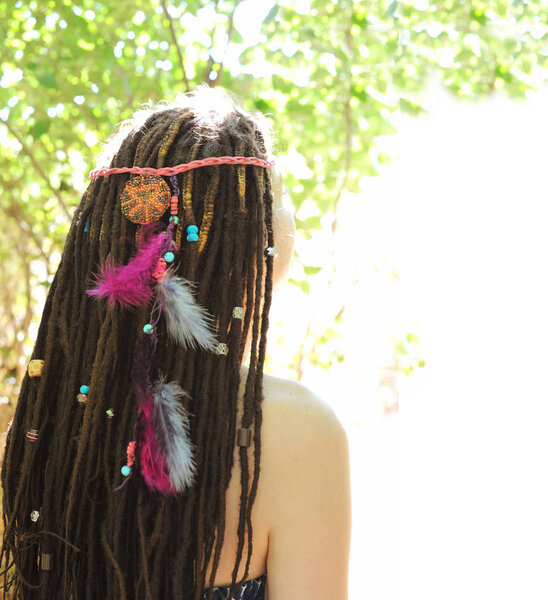 Woman head with dreadlocks hairstyle decorated assorted beads and colored feathers, sunny outdoor, no face