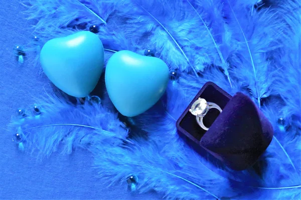 Два блакитних серця і кільце заручин на синьому пташиному пір'їні в дереві — стокове фото