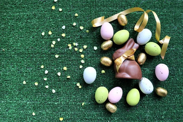 Золотые пасхальные яйца и шоколадный кролик на зеленом фоне — стоковое фото